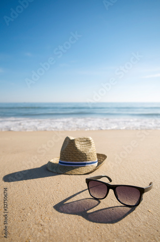 Simple summer hat and cool sunglasses casting long shadows in the setting sun on the smooth sand of an empty beach