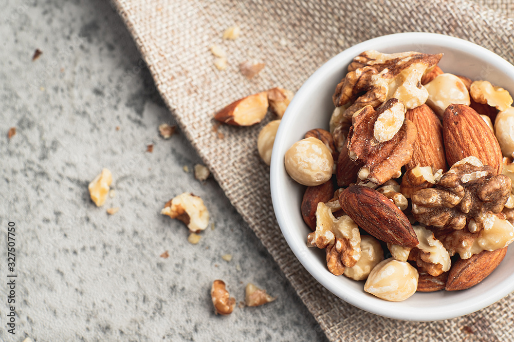 Mixed nuts in white clean bowl on sack cloth contain walnuts, hazelnuts, almonds and macadamia. Healthy food and snack, diet food, concept. Mixed nuts in white clean bowl on sack cloth contain walnuts, hazelnuts, almonds and macadamia. Healthy food and snack, diet food, concept.