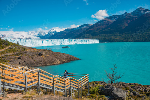 Wonderful view at the huge Perito Moreno glacier and footbridges around with travelers in Patagonia in golden Autumn, South America, sunny day, blue sky