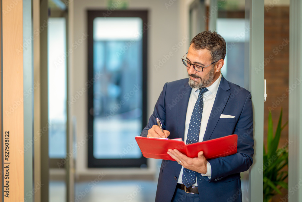 A charismatic, bespectacled bank employee takes notes on his red file A charismatic, bespectacled bank employee takes notes on his red file