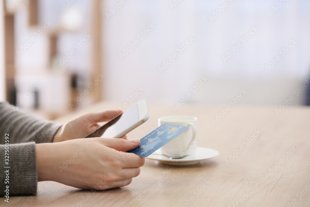 Fototapeta premium Woman using mobile phone for online banking at table