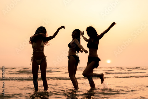 Silhouette of girls were bikini are playing in the sea with happy and funny, sunset in the background. Summer vacation relaxation, travel, nature, happy life unseen concept.