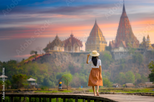 young farmer woman walks on wooden bridge terrace of rice to the temple at morning sunrise with scenerry view of buddhist temple pagoda in background © ID_Anuphon
