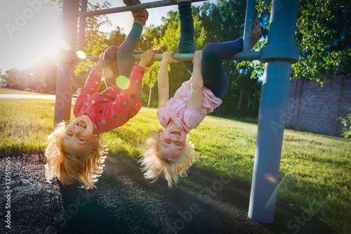 happy cute little girls upside down on monkey bars at sunset