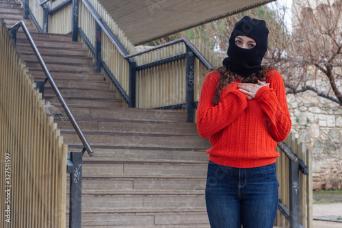 Portrait of attractive caucasian young woman model with ski mask showing shape heart with hands, expressing love, in the park, orange sweater and jeans, long curly hair. Place for your text in copy sp