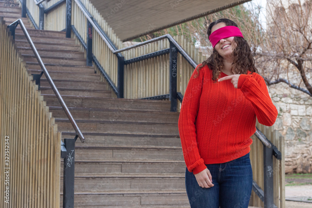 Portrait of attractive young woman model with eye tape pointing aside with cheerful expression, showing something amazing at blank space, in the park, orange sweater and jeans, long curly hair. Place Portrait of attractive young woman model with eye tape pointing aside with cheerful expression, showing something amazing at blank space, in the park, orange sweater and jeans, long curly hair. Place