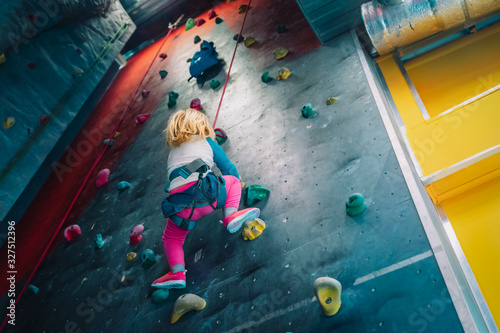 Little girl climbing on artificial boulders wall in gym