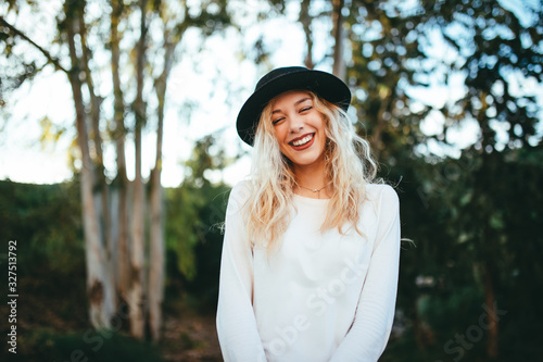 Chica felíz rubia y timida con sombrero en un bosque.