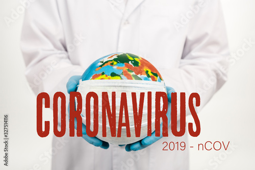 cropped view of scientist holding globe in protective mask near coronavirus, 2019-ncov lettering on white