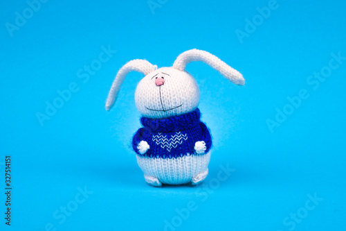 White knitted rabbit, in a blue jacket with a heart, on a blue background. Rabbit with a heart. place for writing. photo