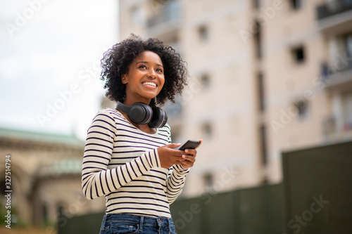 smiling young black woman with mobile phone and headphones outdoor in city