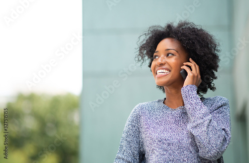 smiling young african American woman talking with cellphone by green wall