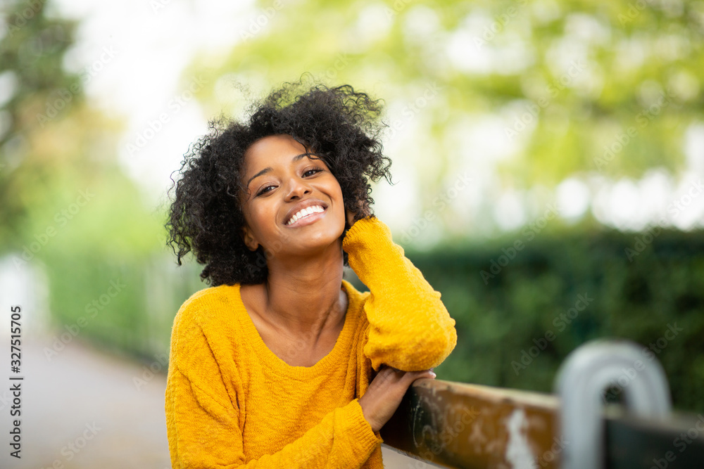 Close up of beautiful young black woman relaxing on bench outside and smiling