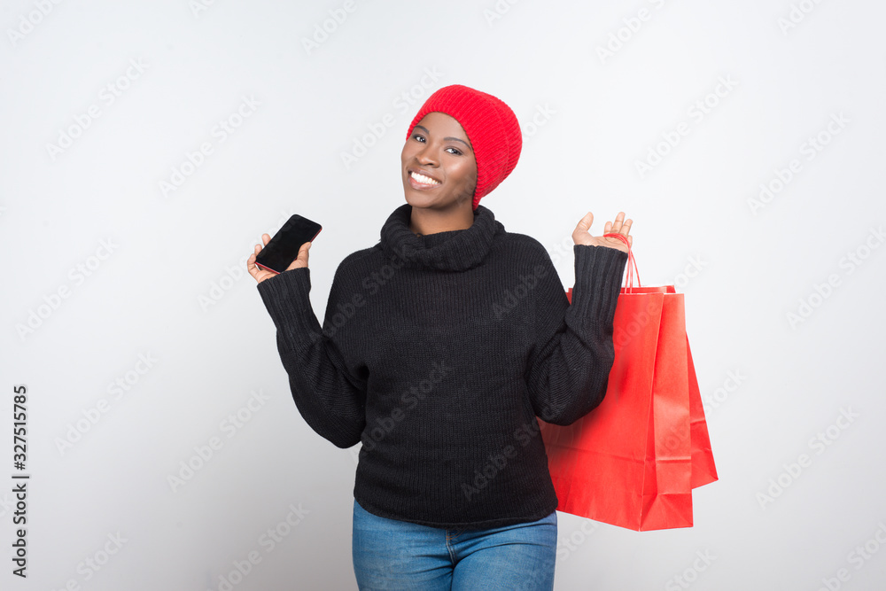 Smiling young woman with shopping bags and phone. Attractive African American lady holding smartphone and paper bags. Shopping, technology concept
