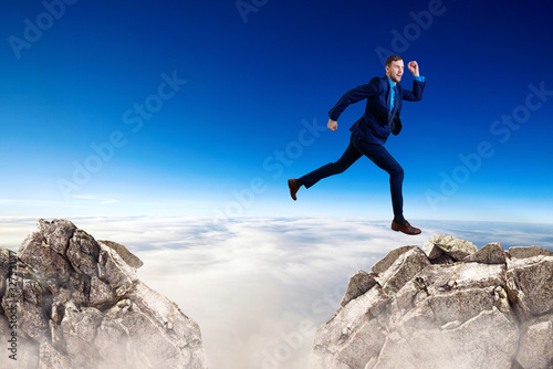 Businessman jumping through the gap among mountains.