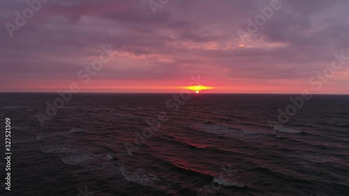 Aerial view of beautiful sunset by the Baltic sea. Red sky with flaming sun, nice waves. Seagull is flying by.