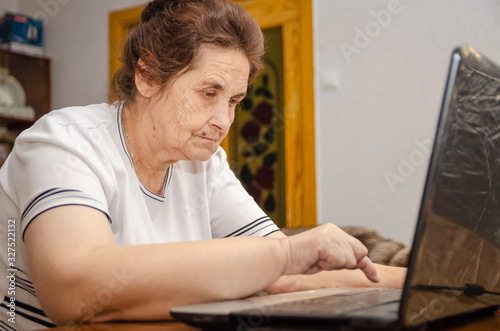 elderly dark-haired woman is sitting at a Desk typing on a laptop