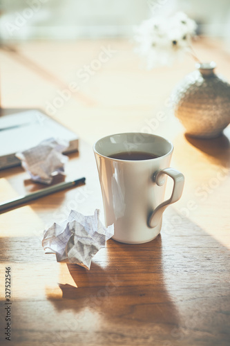 Mug of tea on wooden table with paper balls  pencil and book in background