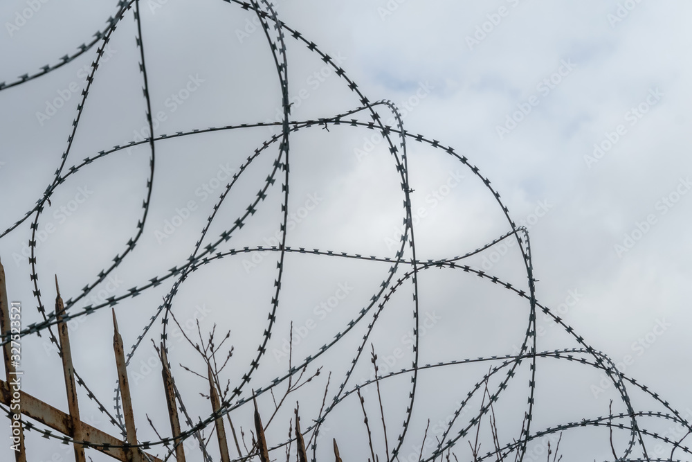 Barbed wire on a fence against a gray sky Barbed wire on a fence against a gray sky