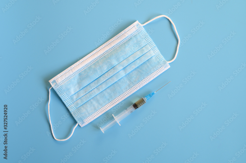protective medical mask blue color and syringe with injection vaccine on a blue background. coronavirus vaccine concept. top view, flat lay protective medical mask blue color and syringe with injection vaccine on a blue background. coronavirus vaccine concept. top view, flat lay
