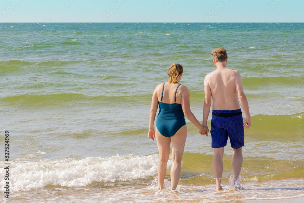 Couple going into sea with wave splashes Couple going into sea with wave splashes