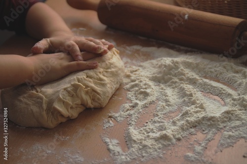 Little backer. Child's hands knead the dough on a wooden table in the kitchen. Easter cake preparation.