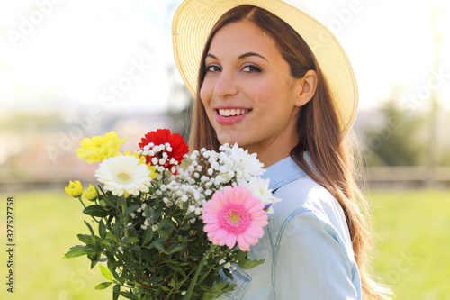 Side view of beautiful smiling teenager girl with flower bouquet looking at camera outdoor