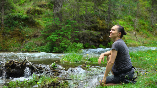 Young hiker woman sitting by a mountain stream  enjoys spending free time at nature