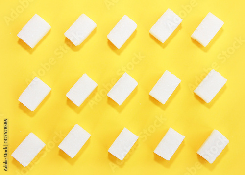 small pieces of natural white refined sugar on a yellow background © Mari