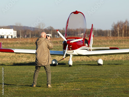 Yaslo, Poland - 7 9 2019: A man is photographing a red sports and tourist red turboprop airplane standing at a grass airfield. Free time at an air show. Private aviation for travel and entertainment photo