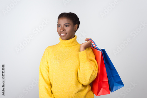 Beautiful cheerful woman holding shopping bags on shoulder. Attractive smiling young lady with paper bags looking at distance. Shopping concept