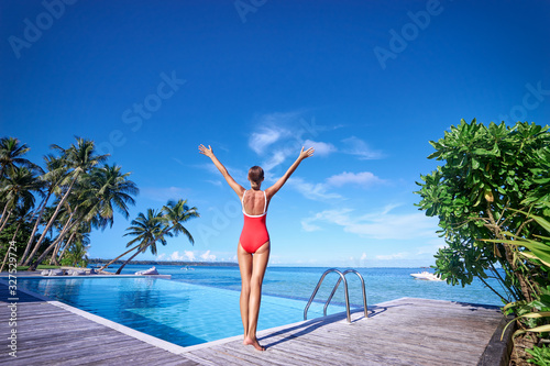 Feel freedom! Young woman in red swimsuit enjoying the view near swimming pool on tropical beach.