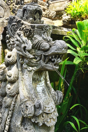 Smiling stone dragon statue among lush tropical foliage outside an ancient temple in Bali Indonesia