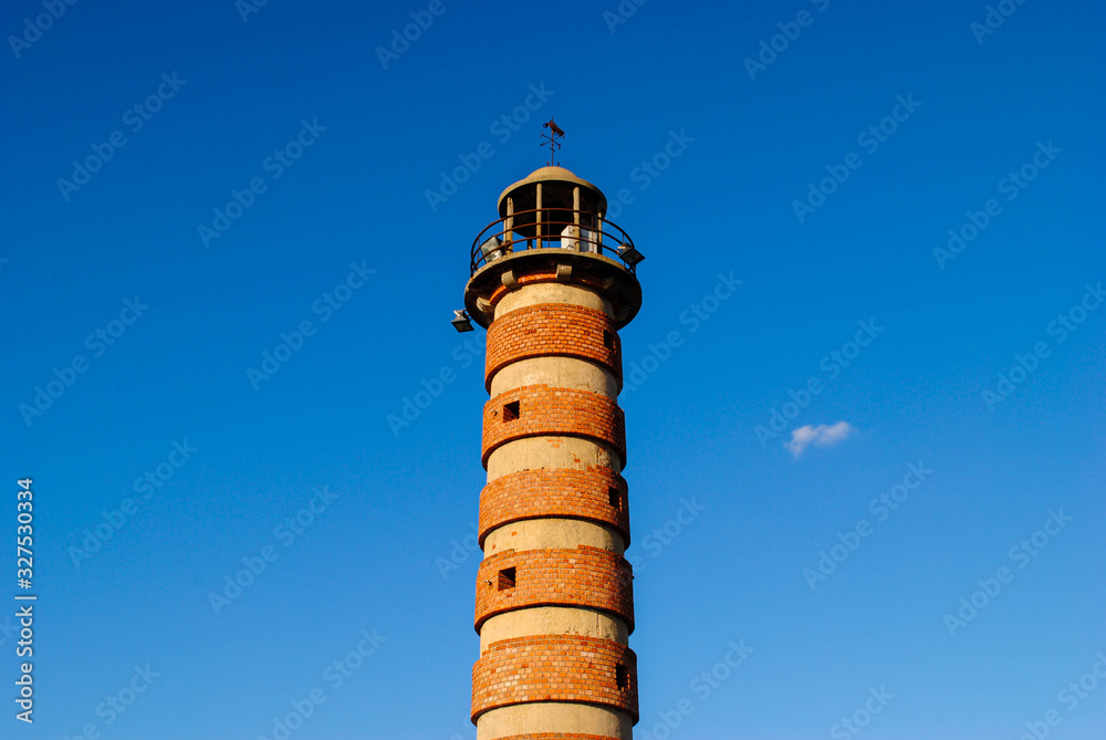 Old red brick lighthouse on a background of blue sky