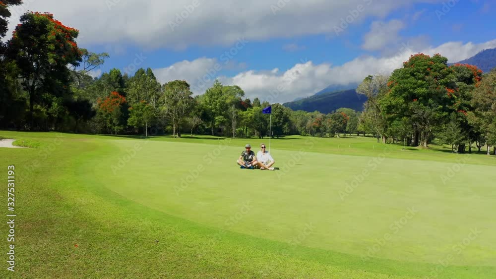 Young couple sitting on a golf course in mountains at the Bali, Indonesia. Aerial view 4K Young couple sitting on a golf course in mountains at the Bali, Indonesia. Aerial view 4K