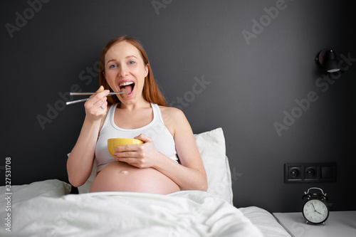 Hunry pregnant woman eating chinese food in bedroom. photo