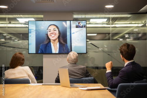 Employees listening to smiling leader during video conference. Business people looking at monitor screen during video conference in office. Business conference concept