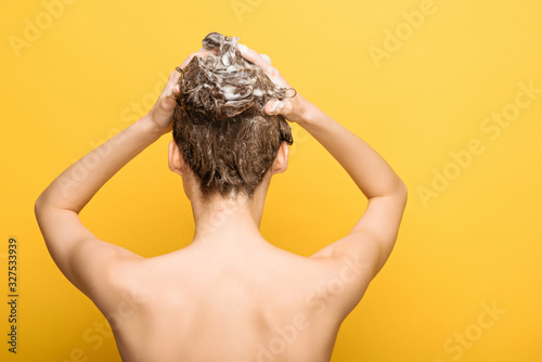 back view of nude woman washing hair with shampoo on yellow background