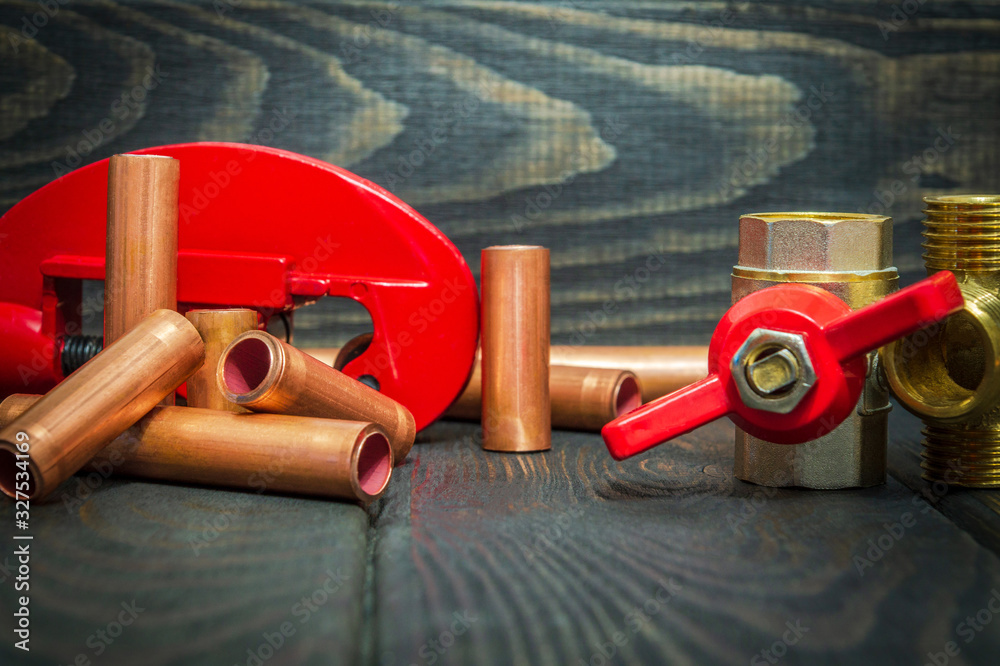 Water ball valve with red handle, brass fittings and copper pipes for plumbing repairs on black vintage wooden boards