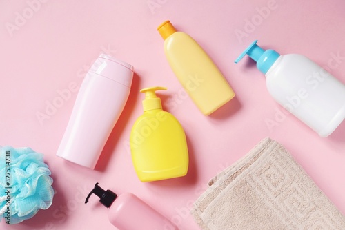 Baby care cosmetic products view from above photography. Blue sponge, shampoo bottle, shower gel packing, hair balm, conditioner, cotton towel on a pink background