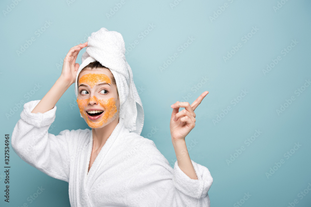 excited girl with citrus facial mask pointing with finger and looking away on blue background excited girl with citrus facial mask pointing with finger and looking away on blue background