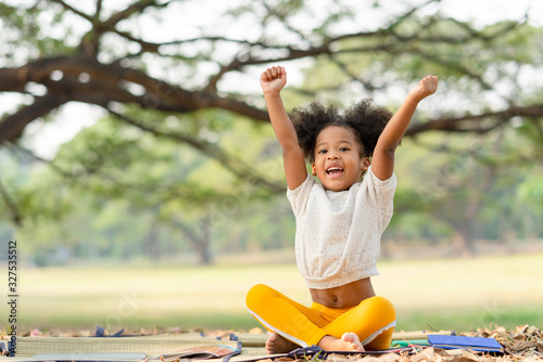 фотографія Happy African american little girl smiling and raises her hand while sitting in