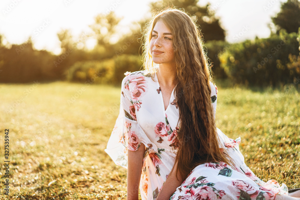 Young girl with long curly hair, brunette, face in freckles, with makeup and green eyes, in light white dress posing for camera, background blurred, nature. Young girl with long curly hair, brunette, face in freckles, with makeup and green eyes, in light white dress posing for camera, background blurred, nature.