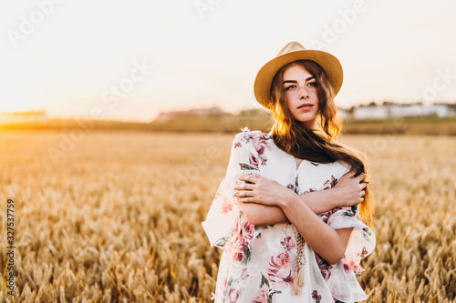 Incredible young woman with long curly hair and freckles face. Woman in dress posing in wheat field at sunset. Close up portrait