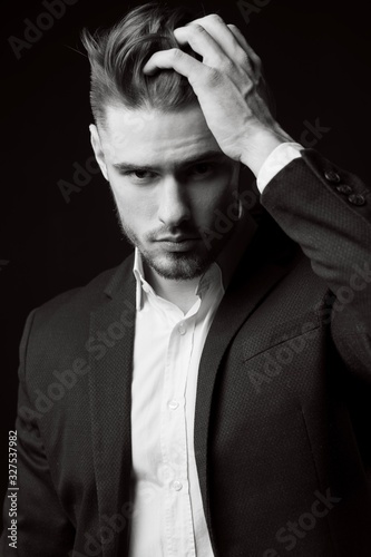 young stylish man with a beard. A man in a classic suit. Male portrait on a black background. Monochrome photo. Male model. Studio business portrait.