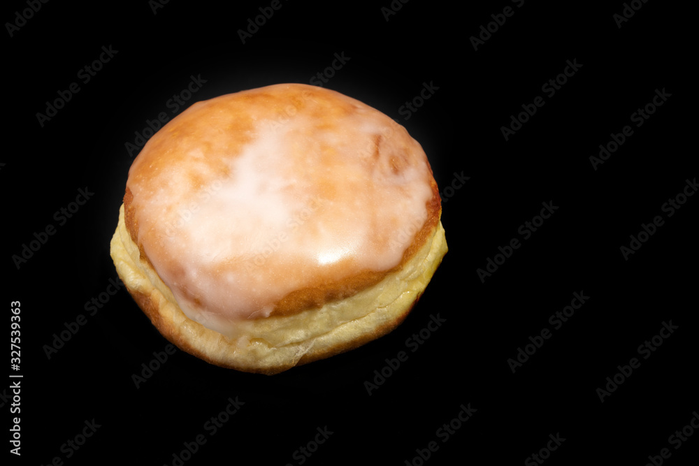 Einzelner Krapfen mit Zuckerguss auf schwarzem Untergrund Einzelner Krapfen mit Zuckerguss auf schwarzem Untergrund