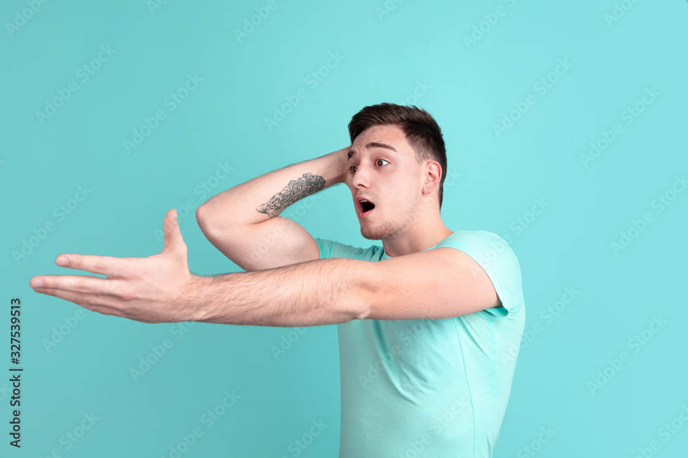 Fototapeta premium Shocked, astonished. Caucasian young man's portrait isolated on blue studio background. Beautiful male model in casual style, pastel colors. Concept of human emotions, facial expression, sales, ad.