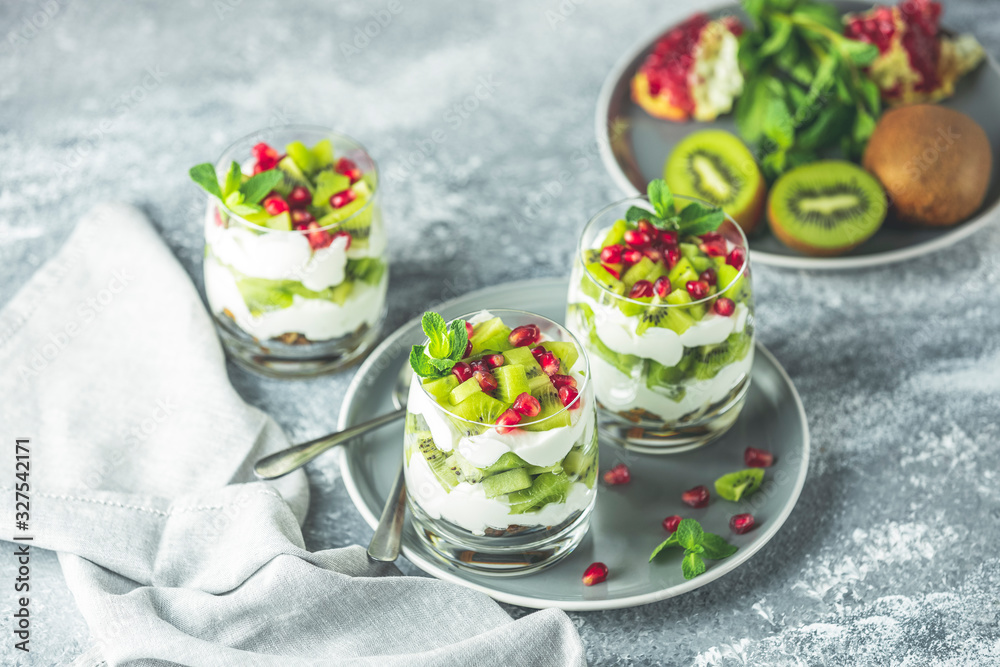 Healthy breakfast: yogurt parfait with granola and kiwi decoration pomegranate and mint on a gray background Healthy breakfast: yogurt parfait with granola and kiwi decoration pomegranate and mint on a gray background
