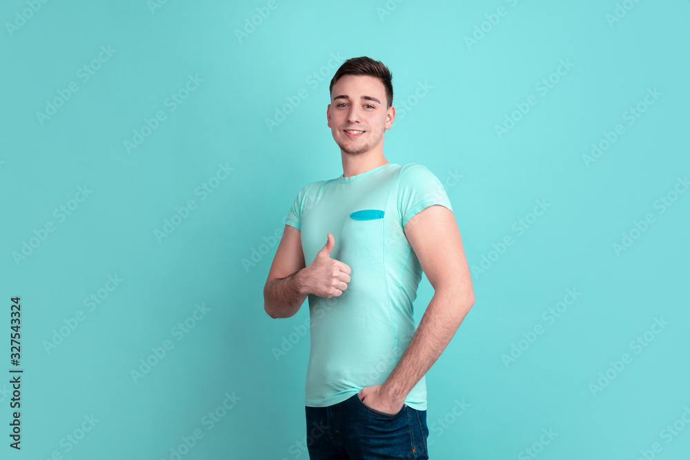 Thumb up, nice. Caucasian young man's portrait isolated on blue studio background. Beautiful male model in casual style, pastel colors. Concept of human emotions, facial expression, sales, ad.