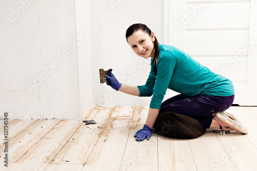 young girl spits on the floor,home repair work,smiling woman putstles the floor and holds a spatula in her hands,filling the wooden floor